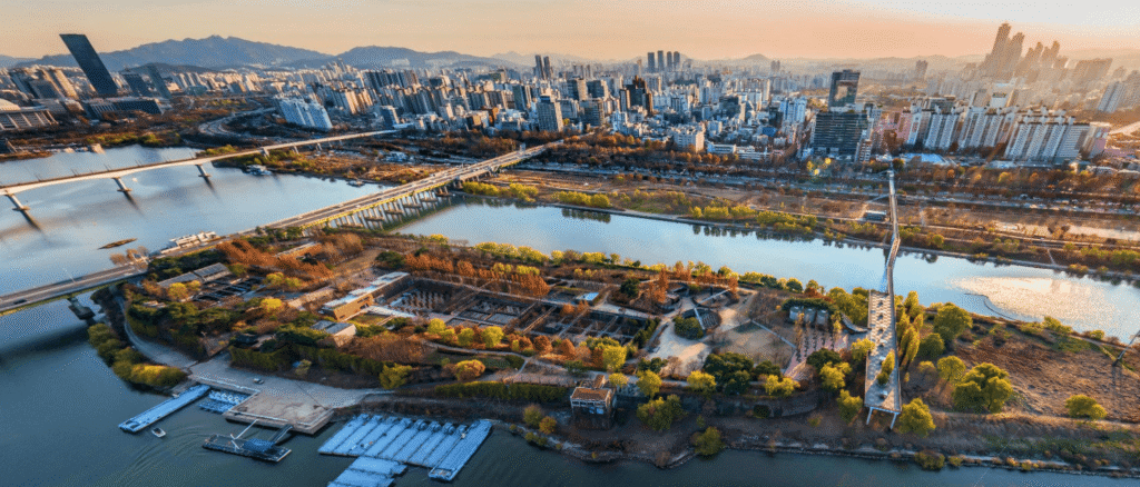 Aerial bird's eye view of Seonyudo Park on the Han River in Seoul during sunset, featuring the bridge and city skyline.